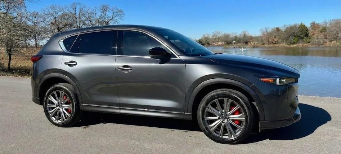 A dark grey 2023 Mazda CX-5 Turbo with dark rims parked by a lake